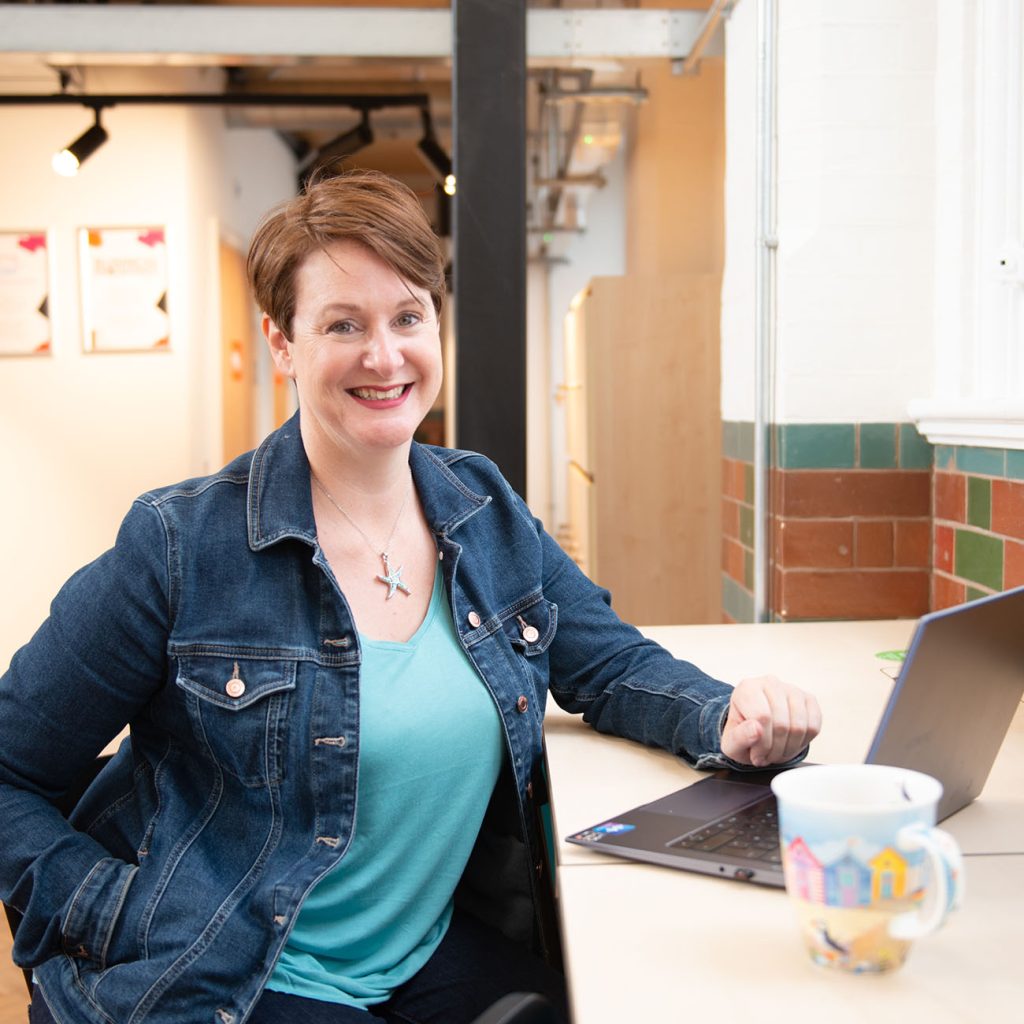 Catherine Jones sat at a desk with laptop and cup of tea